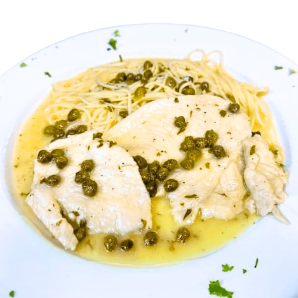 Chicken piccata with capers and linguine pasta in a lemon butter sauce on a white plate.