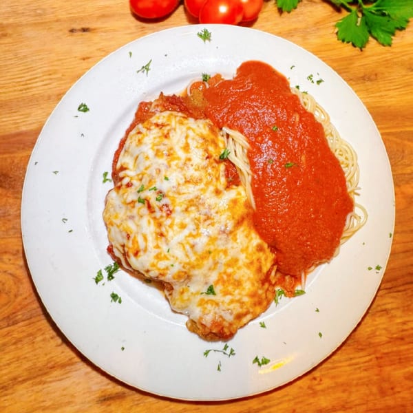 Chicken Parmesan with melted cheese and red sauce, served with spaghetti on a white plate.
