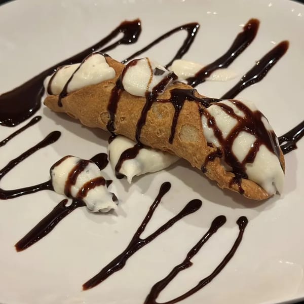 A amore pasta & pizza cannoli dessert drizzled with chocolate sauce on a white plate.