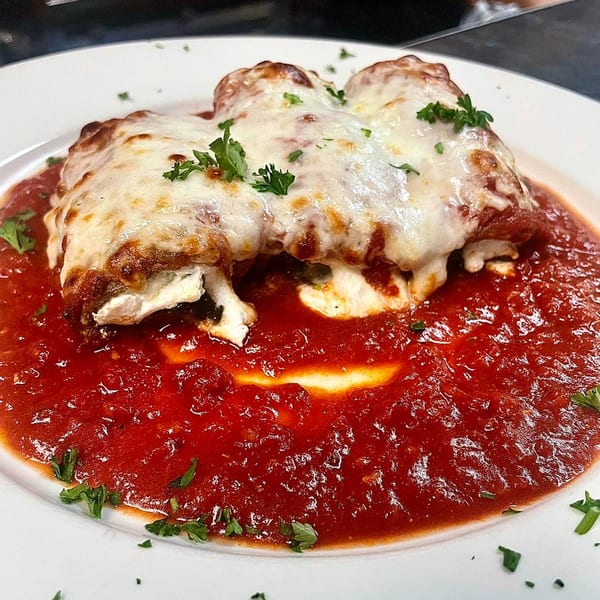 Baked manicotti pasta topped with melted cheese and fresh parsley, swimming in rich red marinara sauce.