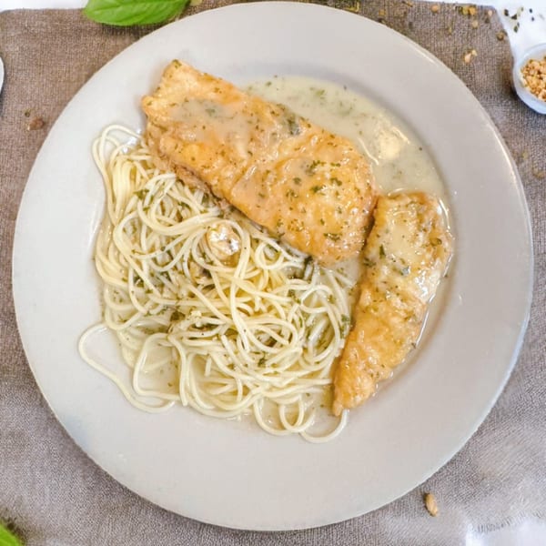 Two pieces of chicken in a creamy sauce with spaghetti on a white plate.