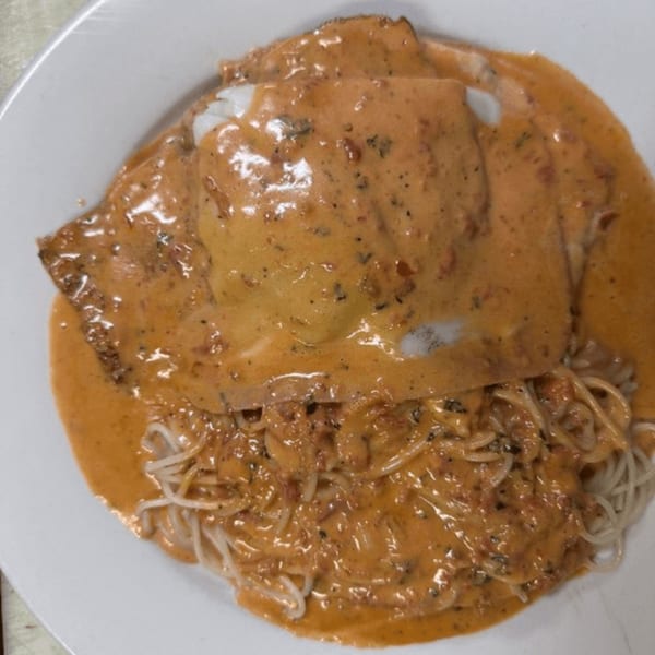 Chicken parmesan with creamy tomato sauce and spaghetti on a white plate.